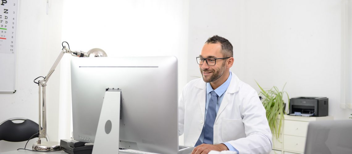 portrait of a handsome man male doctor in medical practice office working on computer